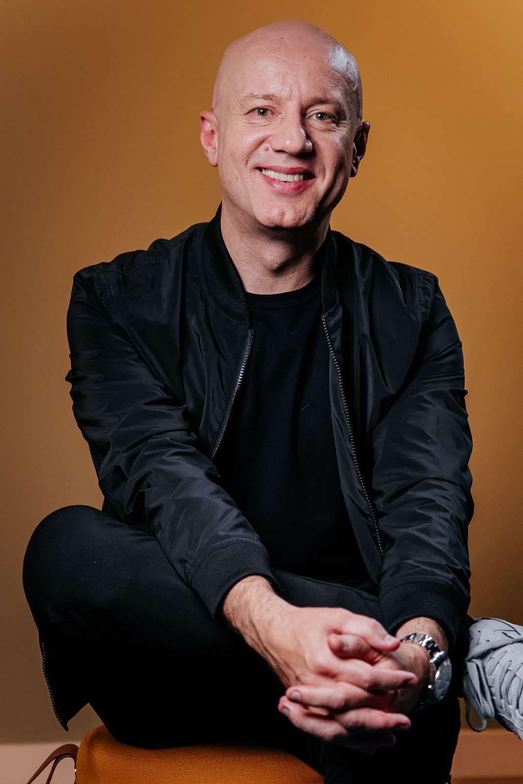 Daniel Keller sentado e sorrindo, de jaqueta preta